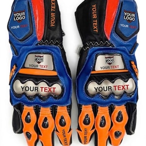 Peut inclure: Une paire de gants de moto noirs, bleus et orange avec des protections pour les articulations. Les gants comportent plusieurs zones marquées du texte YOUR LOGO et YOUR TEXT, notamment sur les doigts, le poignet et la plaque métallique.