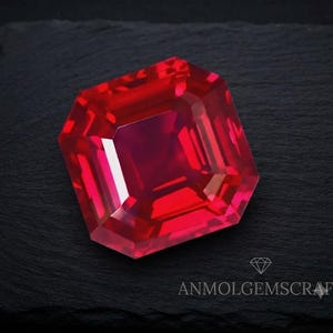Könnte beinhalten: Ein leuchtender, quadratisch geschliffener roter Edelstein mit facettierten Oberflächen, die das Licht reflektieren und tiefe karmesinrote sowie leuchtend scharlachrote Töne erzeugen. Der Stein liegt auf einer dunklen, strukturierten Oberfläche mit dem Text ANMOLGEMSCRAFT und einem Diamantsymbol.