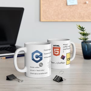 Może przedstawiać: Dwa białe ceramiczne kubki z grafikami o tematyce programistycznej. Jeden kubek przedstawia logo C++, fragmenty kodu, w tym #include <coffee> oraz napis Prompt Engineer Powered by AI. Drugi kubek zawiera logo HTML5 oraz tekst CSS.