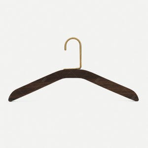 Könnte beinhalten: Ein dunkelbrauner Holzkleiderbügel mit einer glatten, geschwungenen Silhouette und einem messingfarbenen Metallhaken. Das Holz weist eine sichtbare Maserung auf, und der Bügel hat eine breite, konturierte Form zur Unterstützung von Kleidung.