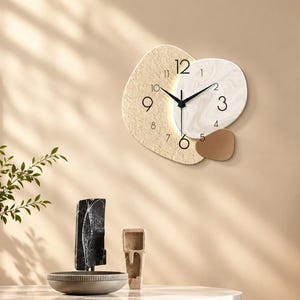 Può includere: Un orologio da parete dal design asimmetrico con tre forme organiche sovrapposte in beige testurizzato, marmo bianco e marrone solido. Il quadrante presenta numeri neri e lancette sottili, con una luce soffusa che emana dal centro.