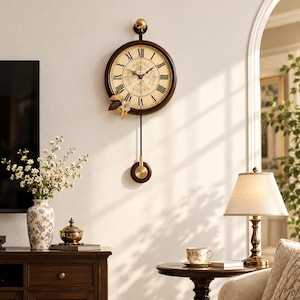 May include: A round wall clock with a dark brown frame, a cream-coloured face featuring black Roman numerals, and a central floral design. A gold-toned pendulum hangs below, and a decorative cluster of gold and brown leaves sits on the lower left.