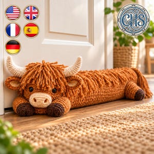 May include: A long, crocheted Highland cow door draft stopper in a warm ginger-brown color. The plush figure features a shaggy mane, cream-colored horns, a light beige muzzle, and dark brown hooves, positioned horizontally on a wooden floor.