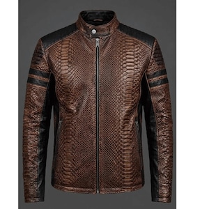 Puede incluir: Una chaqueta marrón con un patrón texturizado de piel de serpiente, que presenta un cuello mao negro, paneles negros en los hombros y mangas negras. La chaqueta tiene un cierre de cremallera central plateado y dos bolsillos laterales con cremallera.