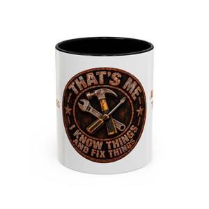 May include: A white ceramic mug with a black rim and handle. The front features a circular, rusted-metal-textured emblem with a crossed hammer, wrench, and screwdriver. The text reads: THAT'S ME, I KNOW THINGS AND FIX THINGS.
