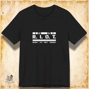 May include: A black short-sleeved t-shirt featuring a white graphic print on the chest. The design includes the text R.I.O.T. in a bold, stencil-style font, with the words REVOLT IT'S ONLY TUESDAY printed in a smaller font directly underneath.