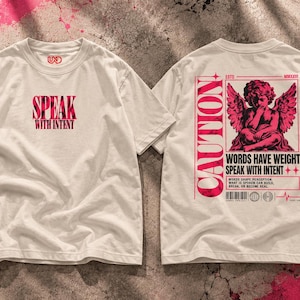 May include: An off-white short-sleeve t-shirt featuring a red graphic on the front that reads SPEAK WITH INTENT. The back displays a red graphic of a winged cherub, the word CAUTION, and the text WORDS HAVE WEIGHT SPEAK WITH INTENT.