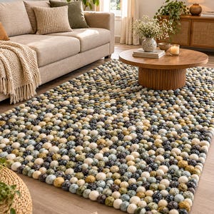 May include: A rectangular area rug composed of numerous small, spherical felt balls in a variegated color palette of cream, sage green, mustard yellow, charcoal gray, and slate blue, creating a textured, multi-dimensional surface.