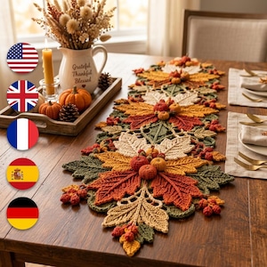 Könnte beinhalten: Ein langer, gehäkelter Tischläufer mit einem sich wiederholenden Muster aus Herbstblättern in Olivgrün, gebranntem Orange, Creme und Gelb, akzentuiert mit kleinen gehäkelten Kürbissen und Beeren, flach auf einem hölzernen Esstisch ausgelegt.