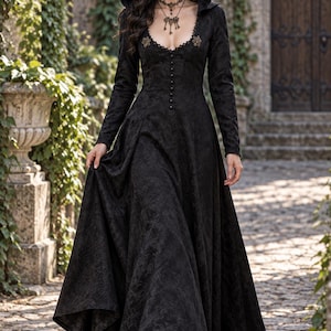 Pode incluir: Um vestido preto comprido até ao chão com capuz, apresentando um padrão floral texturizado, mangas compridas, um decote redondo com acabamento em renda e uma fila de pequenos botões no centro do corpete. A peça inclui dois detalhes metálicos decorativos nos ombros.