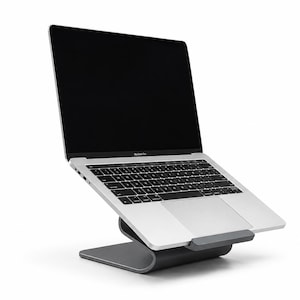 Può includere: Un computer portatile argento con schermo nero è posizionato su un supporto in metallo grigio scuro curvo. Il supporto presenta una base solida e una piattaforma rialzata che mantiene il computer in una posizione inclinata per la visione.