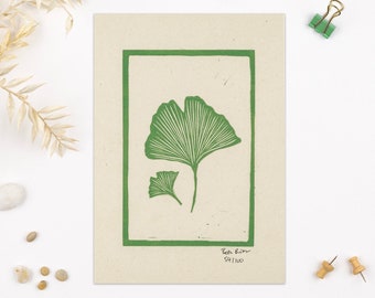 May include: A green ginkgo leaf print on a beige background with a green frame. The print is signed "Tess Gunn" and dated "04/100".