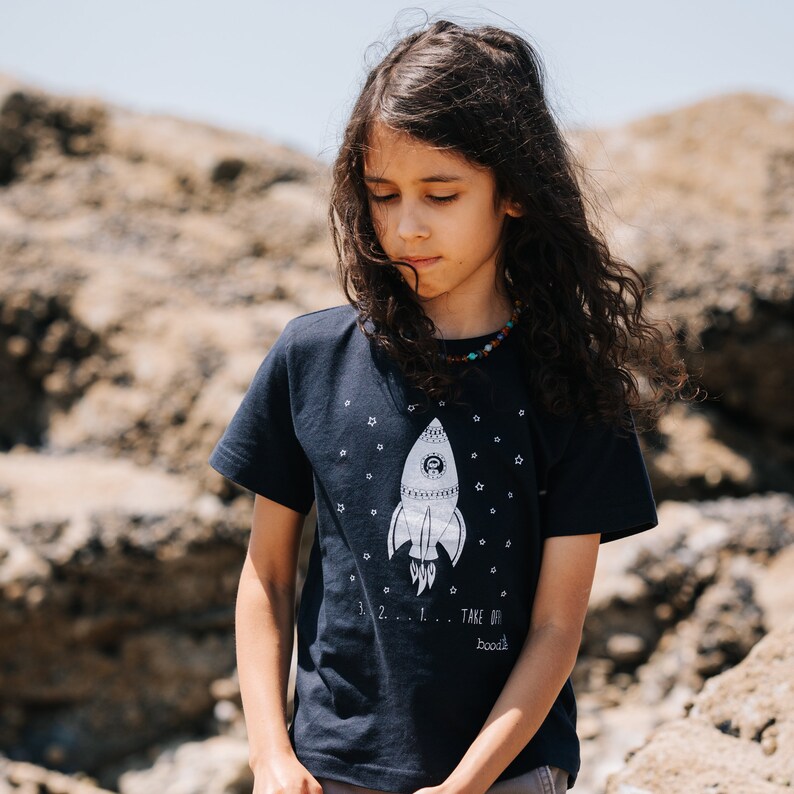 May include: A dark blue t-shirt with a white rocket ship graphic and the text "3...2...1... TAKE OFF!" and "boook!" printed on the front.