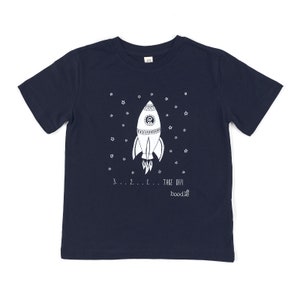 May include: A navy blue t-shirt with a white rocket ship design and the text "3...2...1... TAKE OFF! boodie" printed on the front.