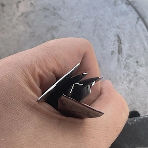 May include: A multi-blade metal tool featuring several sharp, pointed, silver-toned steel blades arranged in a fan-like configuration. The blades are metallic with a smooth, reflective finish and are held together at a central point, showing pointed tips.