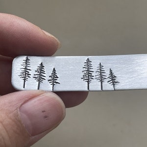 Puede incluir: Una barra de metal plateado con un diseño de seis pinos negros grabados en la superficie.