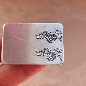 May include: A silver metal stamp with two engraved images of an octopus with tentacles.