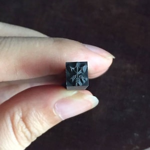 May include: A black metal stamp with a detailed design of a stylized flower.