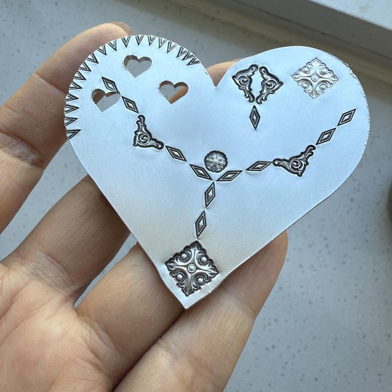 May include: A silver heart-shaped metal pendant with an intricate design of hearts, diamonds, and swirls.