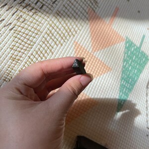 May include: A black metal triangle stamp with a textured surface.