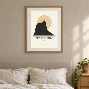 May include: A framed wall art print featuring a minimalist black silhouette of Pendle Hill against a pale cream background with a large peach-colored circle. The text reads PENDLE HILL, 558 m, and coordinates in Lancashire, England, in a wooden frame.