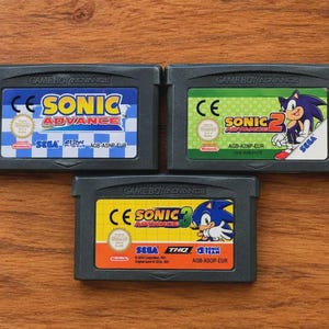 May include: Three grey Game Boy Advance video game cartridges featuring Sonic Advance, Sonic Advance 2, and Sonic Advance 3. Each cartridge has a colourful label with the game title, the Sega logo, the Nintendo seal, and specific model codes.