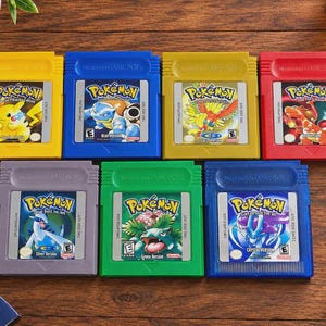 Può includere: Una collezione di sette cartucce per videogiochi Nintendo Game Boy con vari titoli Pokemon, tra cui le versioni Pikachu, Blue, Gold, Red, Silver, Green e Crystal. Ogni cartuccia mostra la sua etichetta di gioco e il titolo.