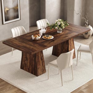 May include: A rectangular dark brown wooden dining table with a thick, solid pedestal base, surrounded by four off-white upholstered chairs with vertical stitching, featuring a glass pitcher, a bowl of bread, and a plate of fruit on top.