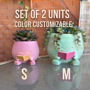 Peut inclure: Un ensemble de deux pots de fleurs en forme de personnages lisant des livres. Le petit pot rose contient une succulente et le grand pot vert menthe contient une plante tombante. Texte : SET OF 2 UNITS, COLOR CUSTOMIZABLE, S, M.