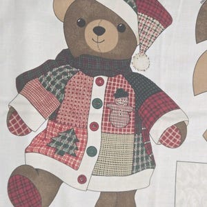 May include: A fabric panel featuring a brown teddy bear wearing a patchwork coat, a dark green scarf, and a matching hat. The coat displays red, green, and white patterns with a snowman and tree graphic. Text at the bottom states: Approximate finished size of bear: 18" tall.