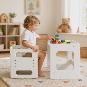 May include: A white wooden learning tower that converts into a table and chair set. The structure features smooth panels, rounded cutouts, and exposed metal hardware, providing a stable platform for play and activities in a neutral finish.