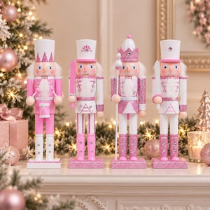 Puede incluir: Cuatro figuras decorativas de cascanueces en tonos rosa y blanco. Cada figura viste un uniforme con detalles brillantes, un sombrero alto y una barba blanca. Se apoyan sobre bases rectangulares, una sostiene un tambor y las otras sostienen bastones.