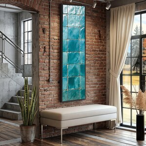 May include: A tall, rectangular wall art piece featuring a grid of glossy, square tiles in varying shades of turquoise, teal, and deep blue, framed in a thin black border and mounted vertically on a textured red brick wall surface.
