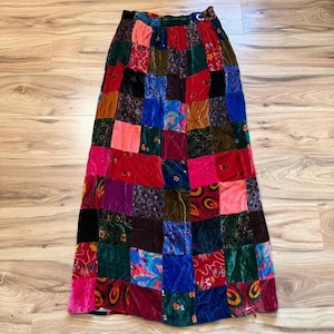May include: A floor-length skirt featuring a patchwork design composed of various square fabric panels. The garment displays a vibrant array of colors including red, blue, green, pink, purple, and black, with diverse textures and patterns.