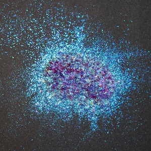 May include: A pile of loose, iridescent craft glitter featuring a vibrant mix of metallic blue, teal, and deep purple flakes. The particles vary in size and shape, creating a reflective, multi-dimensional effect with a high-gloss finish.