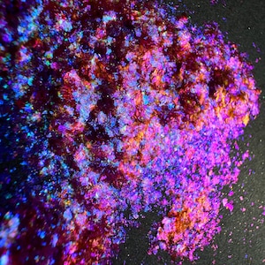 May include: A collection of iridescent, multi-colored flakes featuring a vibrant spectrum of deep purple, magenta, electric blue, and warm orange tones. These thin, reflective particles create a shifting, holographic effect across the surface.