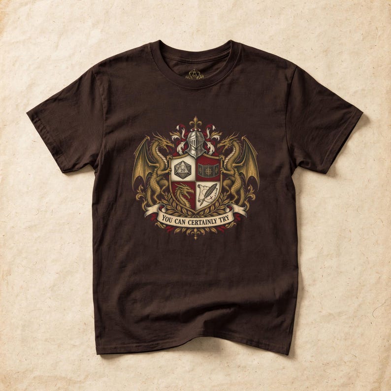 May include: A dark brown short-sleeved t-shirt featuring a central heraldic crest graphic. The design includes two gold dragons, a knight's helmet, and a shield divided into four quadrants with a d20 die, a book, a dragon head, and a quill. The text reads YOU CAN CERTAINLY TRY.