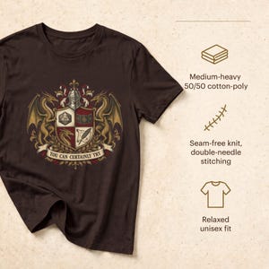 K&ouml;nnte beinhalten: Ein dunkelbraunes T-Shirt mit einem Wappen, das zwei Drachen, einen Ritterhelm und einen Schild mit einem 20-seitigen W&uuml;rfel, einem Buch, einem Drachenkopf und einer Feder zeigt. Der Text lautet YOU CAN CERTAINLY TRY. Mittelschweres 50/50 Baumwoll-Polyester.