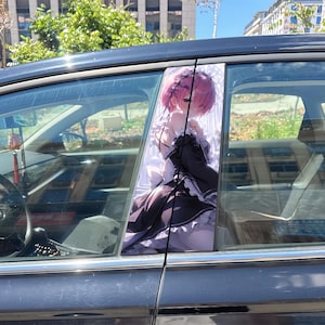 May include: A car window decal featuring an anime-style character with short pink hair, wearing a black and white maid outfit with frills. The character is depicted from the waist up, looking toward the viewer with a soft expression.