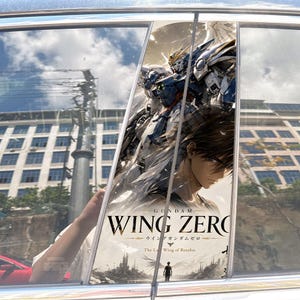 May include: A car window decal featuring a blue and white Wing Zero Gundam robot, a brown-haired character, and the text GUNDAM WING ZERO The Last Wing of Resolve. The design includes a silhouette of a person standing before a ruined landscape.