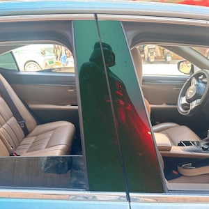 以下が含まれることがあります： タンカラーのレザーシート、ステアリングホイール、黒いセンターピラーを備えた車のインテリア。ピラーの光沢のある黒い表面には、ダース・ベイダーのフィギュアが反射しており、ヘルメットと胸のコントロールパネルがはっきりと映し出されています。