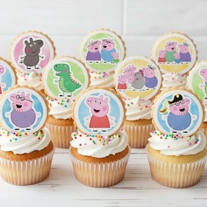 Pode incluir: Uma coleção de cupcakes cobertos com glacê branco, granulado colorido e decorações comestíveis circulares com vários personagens de porquinhos de desenho animado e um dinossauro verde. As decorações mostram a Peppa Pig e sua família.