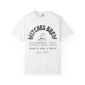 Könnte beinhalten: Ein weißes kurzärmeliges T-Shirt mit einem schwarzen Grafikdruck. Der Text lautet WITCHES BREW COFFEE CO. mit einer zentralen Hexenhut-Illustration, gefolgt von dem Text STOP IN FOR A SPELL und dem kursiven Text Since 1692 unter dem Design.