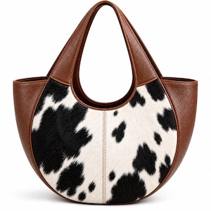 May include: A crescent-shaped handbag featuring a central panel of black and white cow-print hair-on hide. The sides and integrated handles are crafted from smooth brown leather with visible stitching along the curved edges.