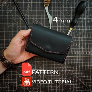 Può includere: Un portafoglio in pelle nera con cuciture rosse, accompagnato da uno strumento per cuoio da 4mm, un filetto con manico in legno e uno stilo nero. L'immagine include il testo PDF PATTERN e YouTube VIDEO TUTORIAL su un tappetino da taglio nero.