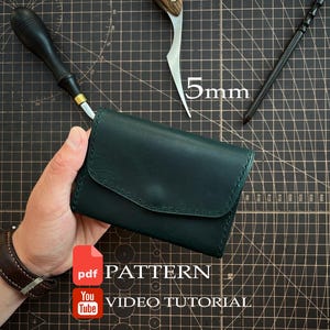 Puede incluir: Una cartera de cuero verde oscuro con cierre de solapa y costuras visibles, acompañada de un cuchillo de rebajar con mango de madera, un lápiz negro y una herramienta negra con punta de metal. Texto: PDF PATTERN y YouTube VIDEO TUTORIAL.