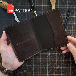 May include: A dark brown leather wallet with visible stitching, featuring multiple interior card slots and a central pocket. The wallet is open, displaying its construction and layout. A red PDF PATTERN icon is visible in the upper left corner.