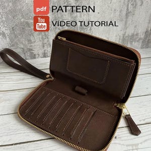 Könnte beinhalten: Eine dunkelbraune Ledergeldbörse mit Handschlaufe, goldenem Reißverschluss, mehreren Kartenfächern und einer Stiftschlaufe. Das Bild enthält den Text PDF PATTERN und VIDEO TUTORIAL, was auf eine Anleitung zur Herstellung des Artikels hinweist.
