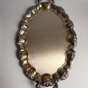 Può includere: Un vassoio da portata ovale color argento con una superficie centrale lucida e un bordo smerlato decorativo caratterizzato da motivi floreali in rilievo. Il vassoio include due manici curvi e ornati alle estremità opposte.