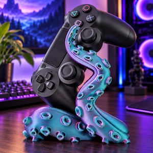 May include: A black video game controller resting on a teal and purple octopus tentacle stand. The tentacle features a gradient color shift with visible suction cups along its length, providing a stable base for the controller to sit upright.